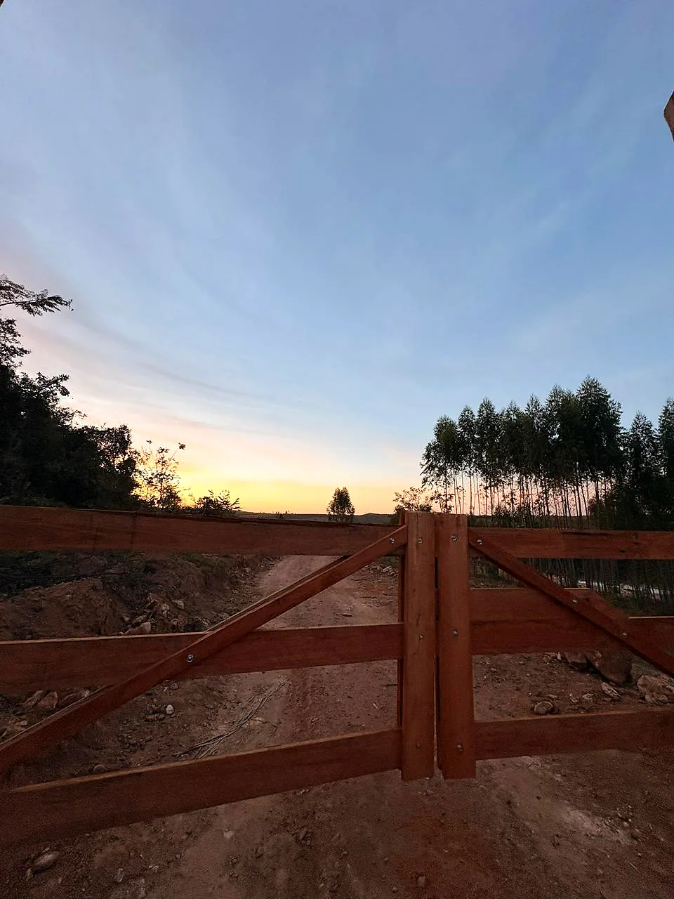 A porteira de madeira da fazenda da AF aberta para a estrada, ao crepúsculo